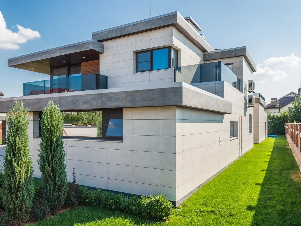 A narrow strip of green lawn beside a modern concrete house and tall evergreens