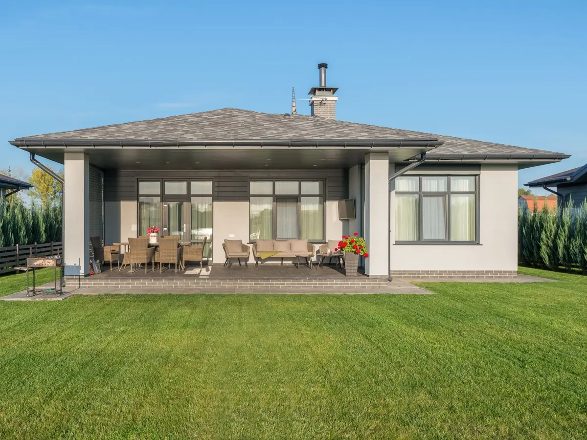 A lush green back lawn in front of a single-story house with a covered patio