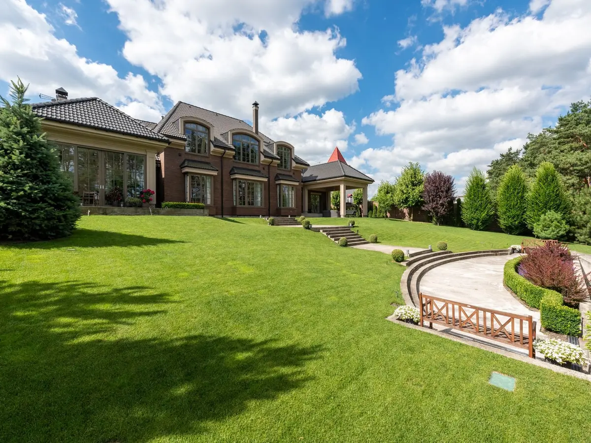A wide green lawn and curved steps in front of a brick house under a blue sky