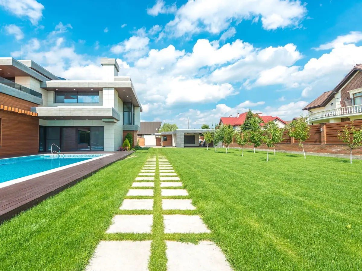 A striped green lawn with a stepping-stone path beside a pool and a modern house
