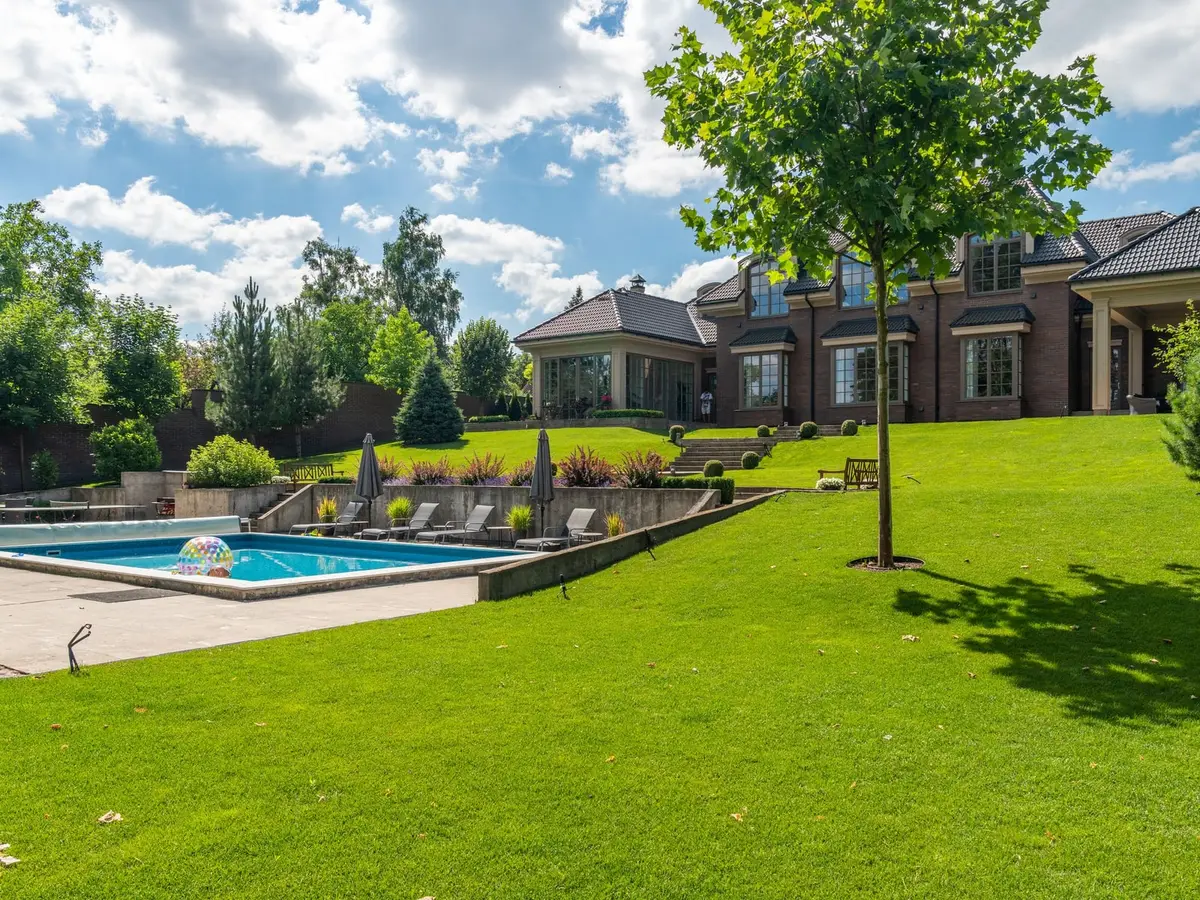 A sloping green lawn rising toward a brick house, with a pool along the lower edge