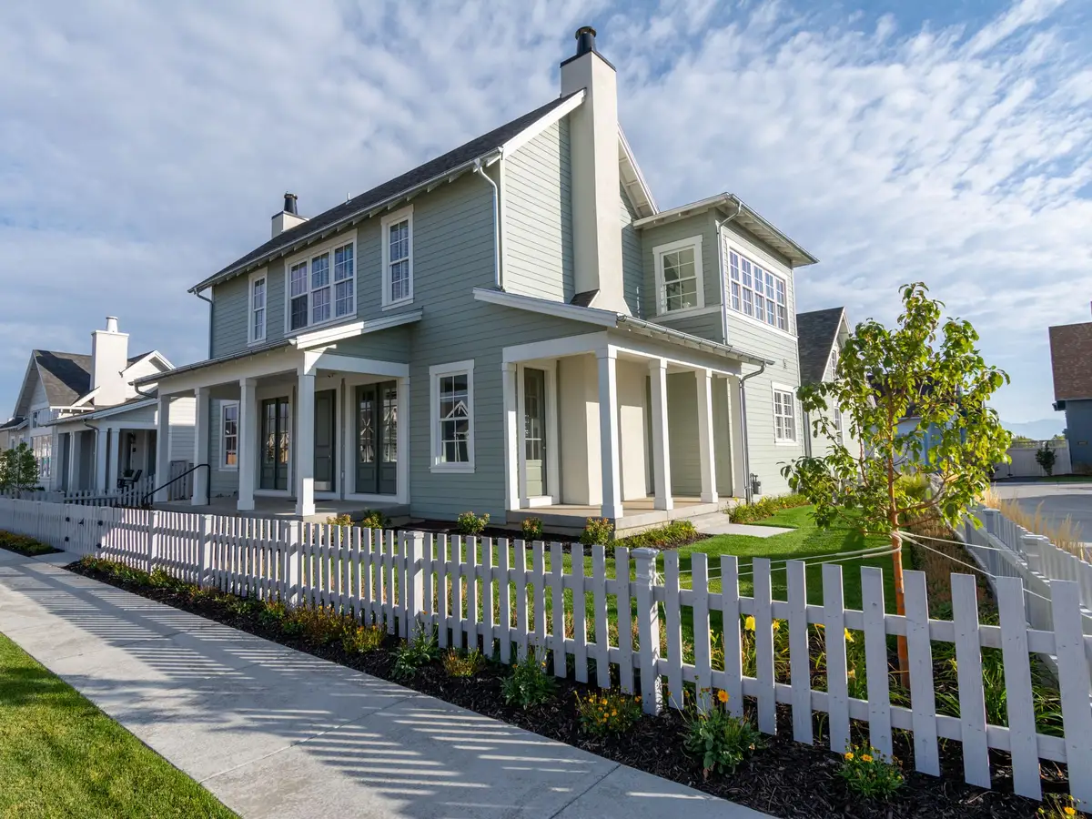 A sidewalk and white picket fence in front of pale houses with narrow strips of lawn