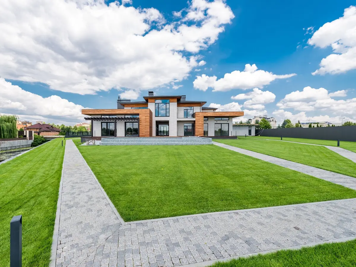 A wide striped green lawn and stone walks in front of a modern house under a bright sky