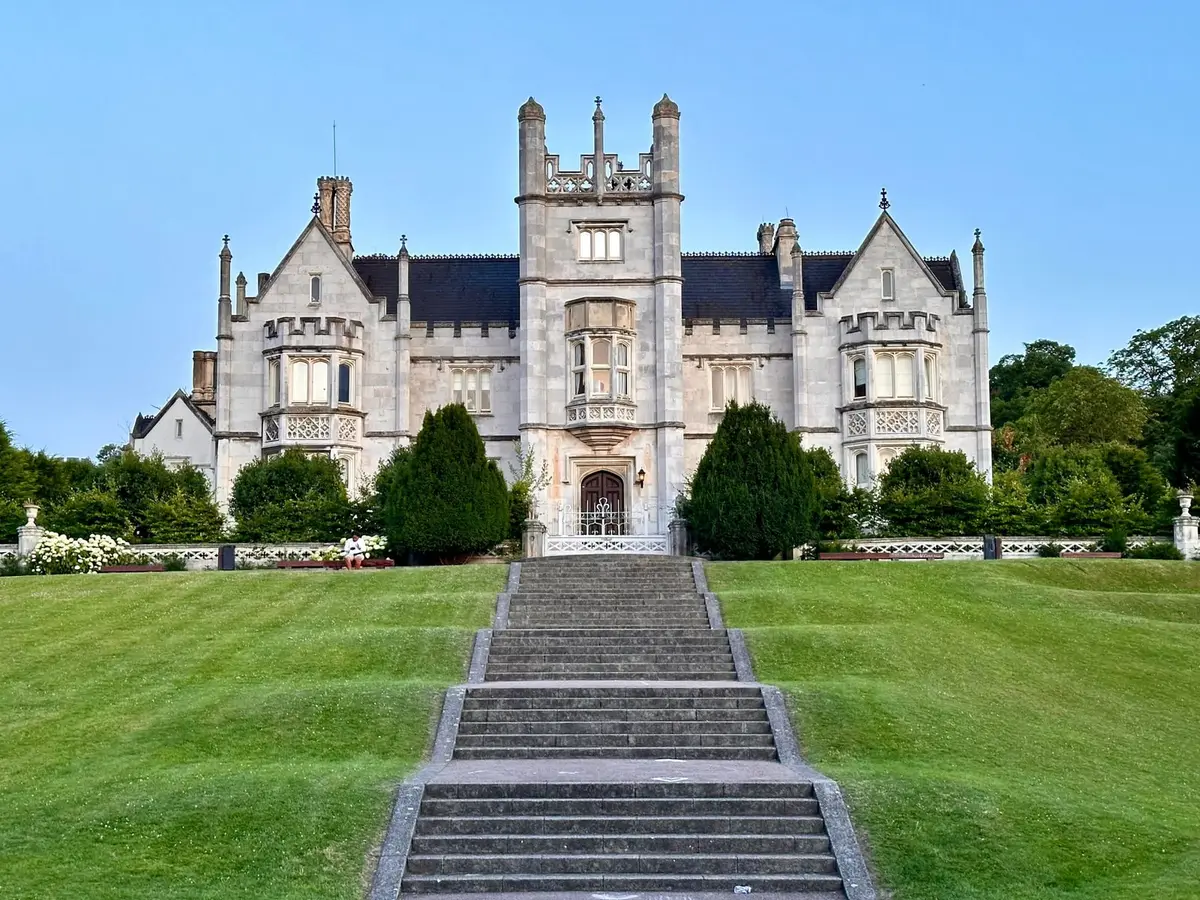 A stone mansion with a wide green lawn and a central stone stair under a clear sky