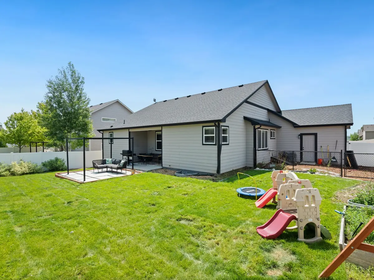 A bright green backyard with a patio, a playset, and a gray house under a blue sky