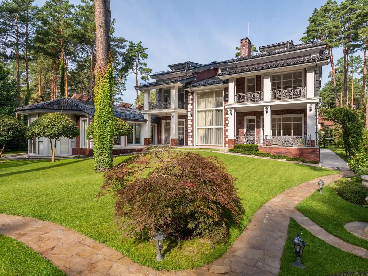 A brick-and-white house with a curved green lawn, stone paths, and pines