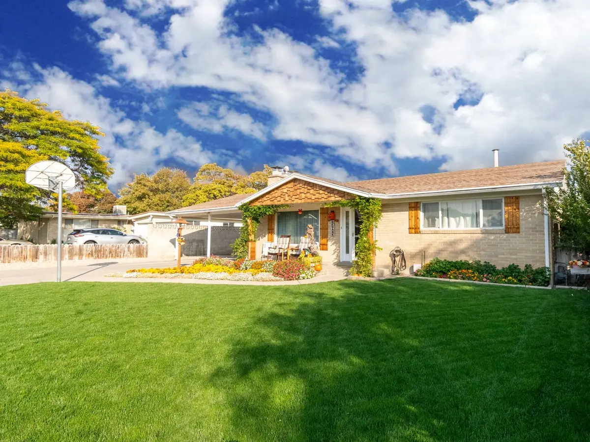 A brick ranch house with a striped green front lawn, a basketball hoop, and flower beds under a blue sky