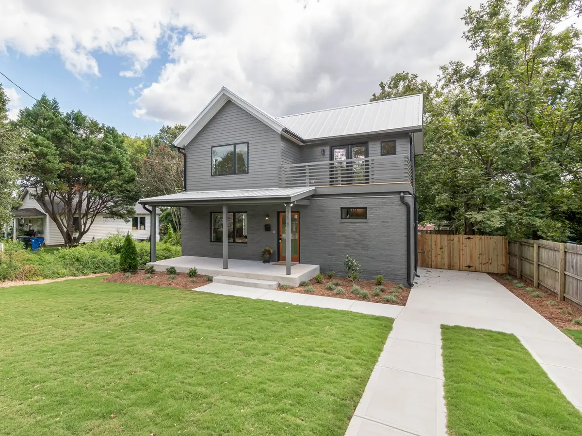 A gray two-story house with a green back lawn, a concrete walk, and a wooden fence