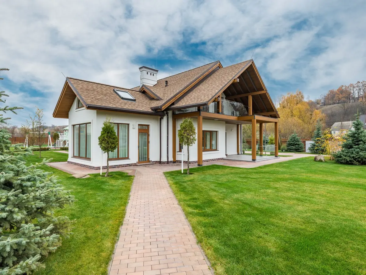 A white cottage with a brick path and a green lawn under a partly cloudy sky