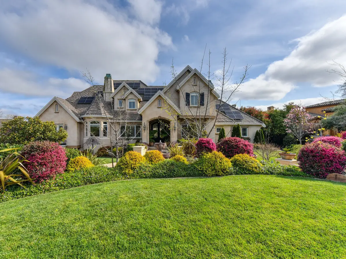 A bright green front lawn sloping up to a house with solar panels and beds of pink and yellow shrubs