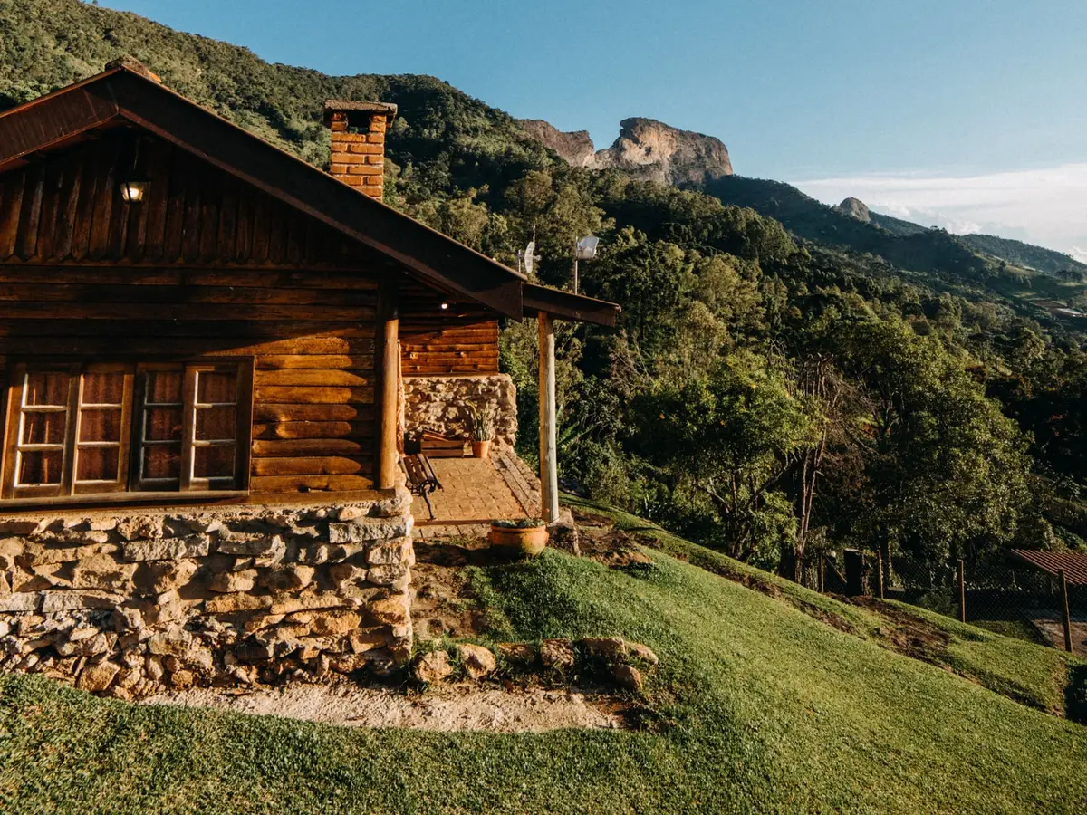 A green lawn beside a log cabin on a wooded hillside under a blue sky