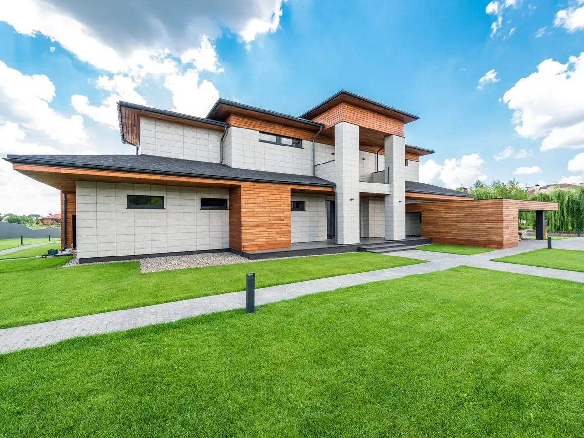 A modern wood-and-tile house with green lawns and paved walks under a blue sky