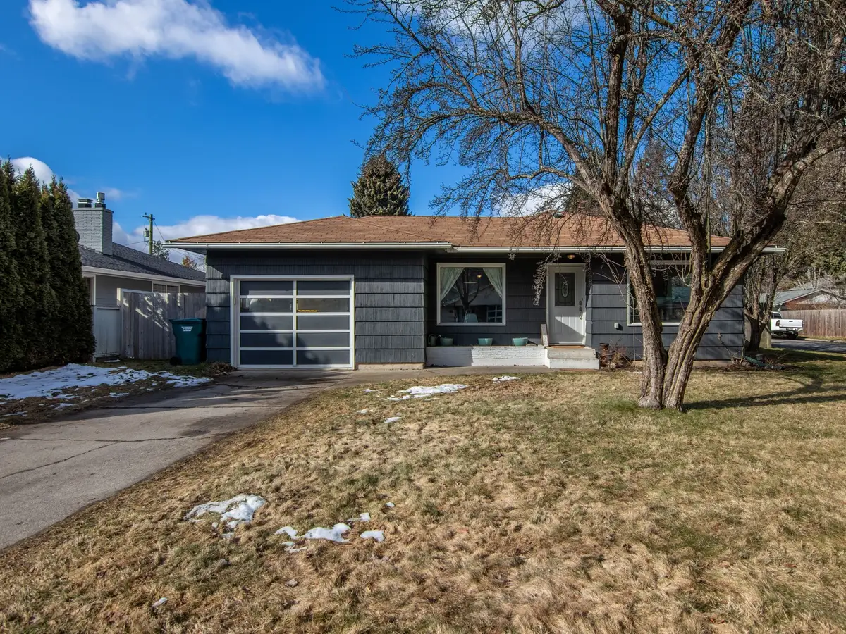 A front yard of dormant brown grass with patches of snow, a bare tree, a dark single-story house, and a white pickup at the right